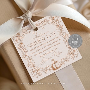 May include: A gift tag with the text "Autumn Simmer Pot" in elegant script, surrounded by floral illustrations. The tag is tied with a cream-colored ribbon, and the gift is wrapped in tan paper.