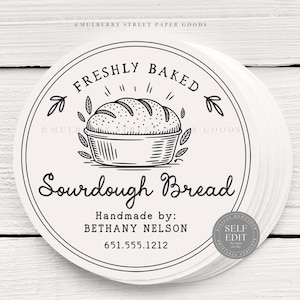 Puede incluir: Una pila de etiquetas redondas de color blanquecino con una ilustraci&oacute;n en negro de una hogaza de pan de masa madre en una cesta. El texto "FRESHLY BAKED" y "Sourdough Bread" se muestran en un dise&ntilde;o circular. Las etiquetas tambi&eacute;n incluyen "Handmade by: BETHANY NELSON" y un n&uacute;mero de tel&eacute;fono.