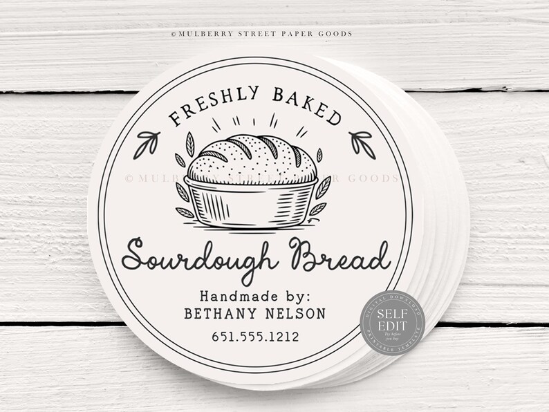 Puede incluir: Una pila de etiquetas redondas de color blanquecino con una ilustraci&oacute;n en negro de una hogaza de pan de masa madre en una cesta. El texto "FRESHLY BAKED" y "Sourdough Bread" se muestran en un dise&ntilde;o circular. Las etiquetas tambi&eacute;n incluyen "Handmade by: BETHANY NELSON" y un n&uacute;mero de tel&eacute;fono.
