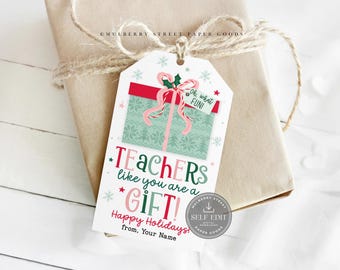 May include: A gift tag with a festive design, featuring a red and green present illustration with a pink bow. Text reads "TEACHERS like you are a GIFT!" and "Happy Holidays!" The tag is attached to a wrapped gift with twine.