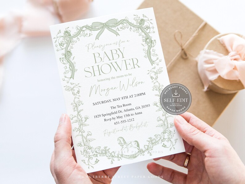 May include: A baby shower invitation with a floral design in light green. The invitation includes the text "BABY SHOWER" and event details. The invitation is held in hands, with a gift box and ribbon in the background.