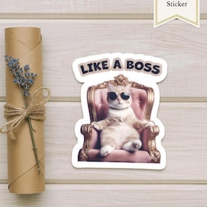 Könnte beinhalten: Ein Aufkleber mit einer Katze mit Sonnenbrille, die in einem rosa Sessel sitzt. Der Text "LIKE A BOSS" steht über der Katze. Links ist eine Rolle braunes Papier mit einem Lavendelzweig, der mit Bindfaden gebunden ist. Rechts ist ein "Handmade Sticker"-Etikett.