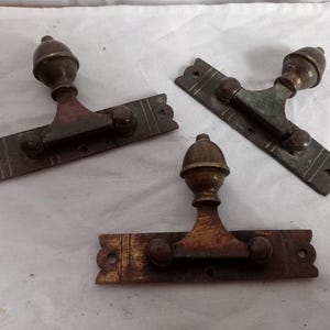 May include: Three antique bronze door latches. Each latch features a decorative finial, a rectangular base with etched lines, and two small knobs. The metal has a weathered, aged appearance, with variations in color from bronze to a reddish-brown.