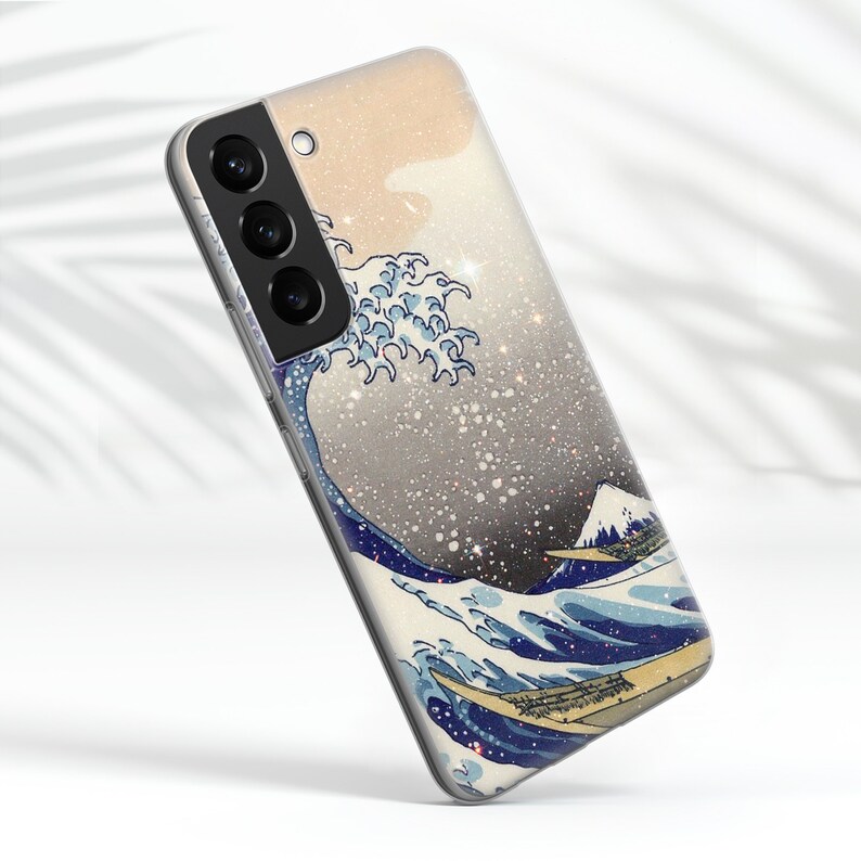 Puede incluir: Una funda para tel&eacute;fono con un fondo plateado brillante y una imagen azul y blanca de una ola. La funda tiene un recorte para la c&aacute;mara con tres lentes.