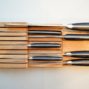 May include: A wooden knife block with eight slots holds a set of kitchen knives with black handles. The knives are arranged in order of size, with the largest knife at the top and the smallest knife at the bottom.