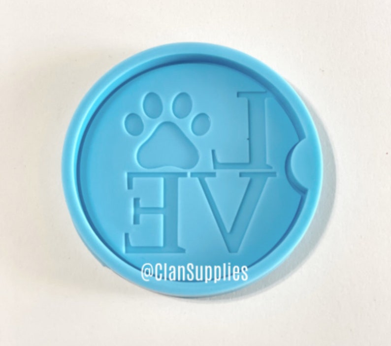 May include: Light blue silicone coaster mold with the word "LOVE" and a paw print in the center. The mold is for making resin coasters. The text "@ClanSupplies" is at the bottom of the mold.