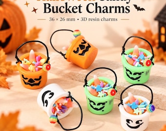 Może przedstawiać: Zestaw zawieszek z żywicy 3D w kształcie wiaderek na słodycze na Halloween o wymiarach 36 x 26 mm. Pomarańczowe, zielone i białe wiaderka mają czarne twarze dyni i są wypełnione kolorowymi cukierkami kukurydzianymi oraz posypką w kształcie gwiazdek.