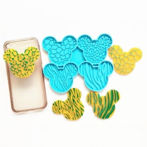 May include: A set of six silicone molds shaped like Mickey Mouse ears. Each mold features a different animal print design: leopard, zebra, giraffe, and cheetah. The molds are blue and the prints are yellow and green.