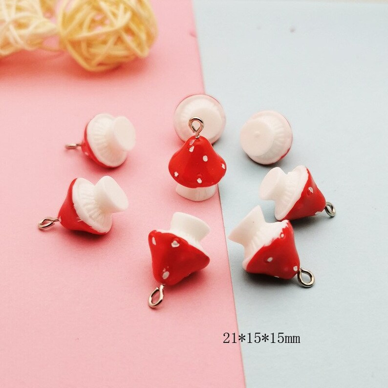 May include: A collection of seven small mushroom charms, each featuring a red cap with white spots and a white stem. Several charms include a small metal loop at the top for attachment. The text 21*15*15mm is visible, indicating the dimensions.