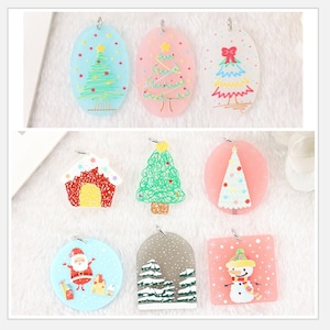 May include: Nine Christmas-themed ornaments with various designs, including a house, a snowman, a Santa Claus, and several Christmas trees. The ornaments are made of clear plastic and have a painted design.