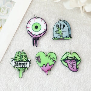 May include: Five colorful charms with a Halloween theme. The charms are made of acrylic and feature a green brain with the word "Zombie" on a banner, a green heart with pink stitching, a green eyeball with pink veins, a green hand reaching out of a gray tombstone with the words "RIP" on it, and a green tongue sticking out of a pink mouth.