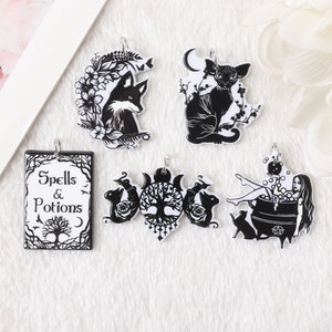 May include: Five black and white charms with a witchy theme. The charms feature a fox, a cat, a tree of life, a book that says "Spells & Potions", and a witch bathing in a cauldron.