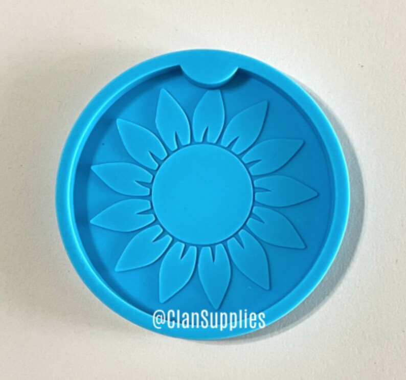 May include: Blue silicone coaster mold with a sunflower design. The mold has a cutout for a cup or glass. The mold is made by @ClanSupplies.