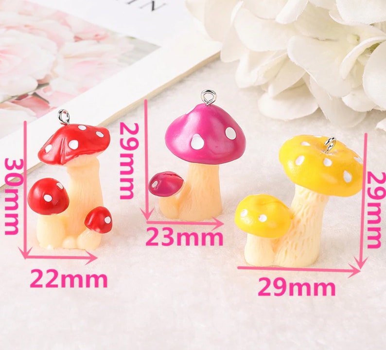 May include: Three mushroom charms with metal loops. The red mushroom set measures 30mm by 22mm. The pink mushroom set measures 29mm by 23mm. The yellow mushroom set measures 29mm by 29mm. Each mushroom features a light-colored stem and a spotted cap.