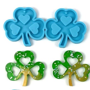 May include: Two blue silicone molds shaped like shamrocks with three heart-shaped cutouts in each leaf. Two finished resin shamrocks with green and gold glitter.