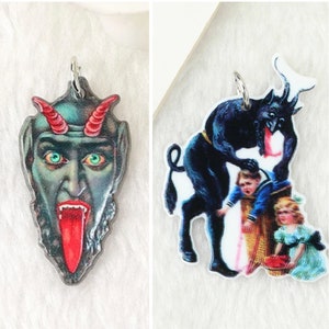 May include: Two vintage-style Christmas ornaments featuring a green and red devil with a long tongue and a black devil with horns and a red tongue, holding a child.