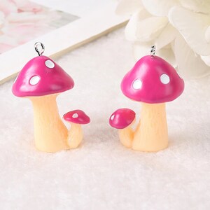 May include: Two mushroom charms featuring bright pink caps with white spots and pale beige stems. Each charm includes a smaller secondary mushroom attached to the base and a small silver metal loop at the top for hanging or attaching to jewelry.
