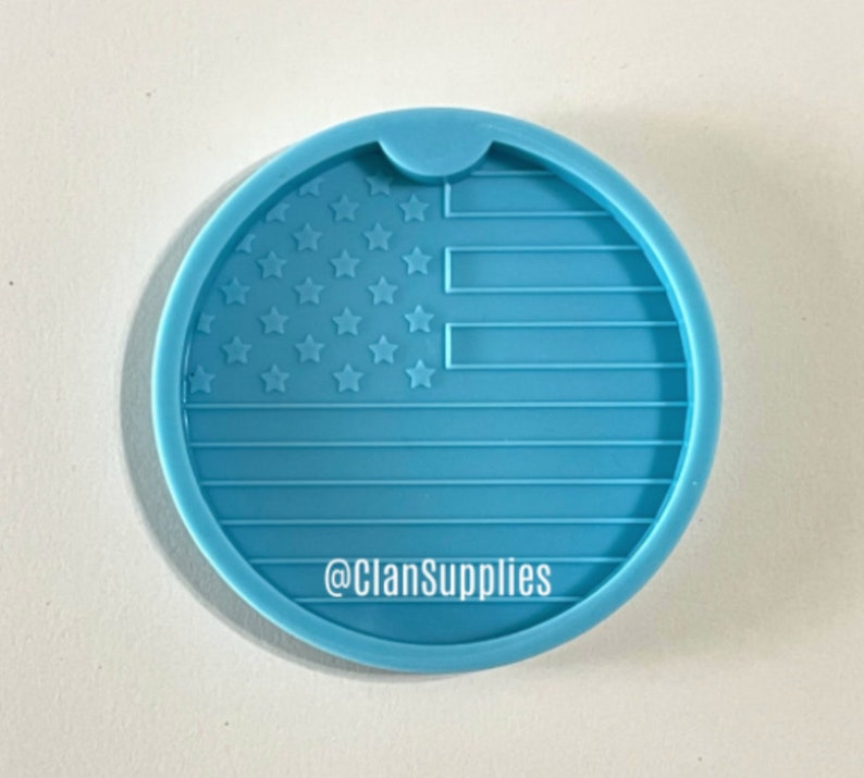 May include: A light blue silicone coaster mold with a raised design of the American flag. The mold has a cut-out for a cup or glass. The text "@ClanSupplies" is printed on the mold.