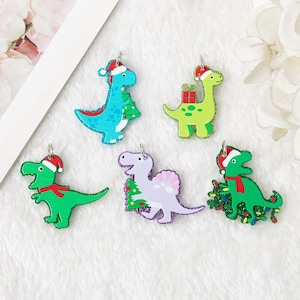May include: Five Christmas-themed dinosaur ornaments. Each dinosaur is wearing a Santa hat and has a different color and design. The dinosaurs are holding Christmas trees, presents, and lights.
