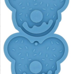 May include: Two blue silicone molds shaped like donuts with sprinkles. Each mold has a hole in the center and two ear-like shapes on the top.