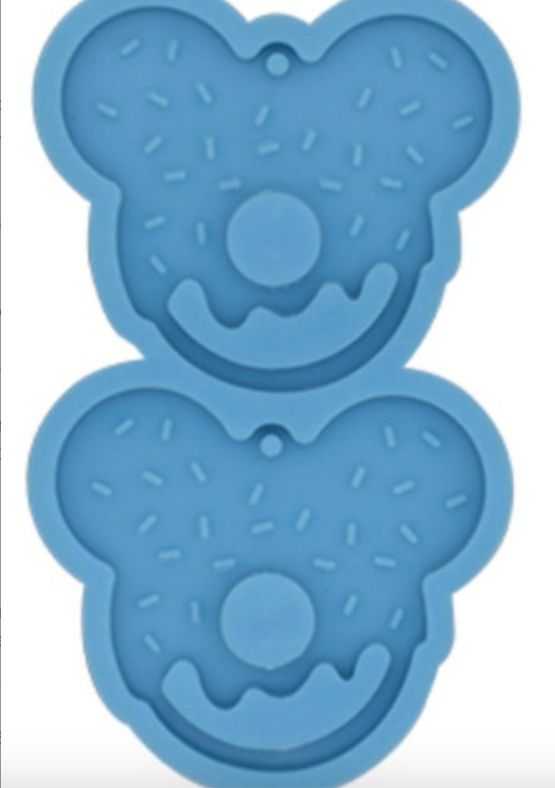 May include: Two blue silicone molds shaped like donuts with sprinkles. Each mold has a hole in the center and two ear-like shapes on the top.