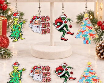 May include: A set of eight acrylic dangle earrings featuring four distinct Christmas designs: a green character dressed as a tree, a Santa Claus face with the text HO HO HO, a green character holding an ornament, and a tree with dinosaur silhouettes.