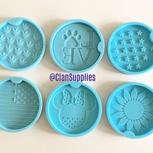 May include: Six round silicone molds for making coasters. The molds feature various designs including a paw print with the word "Love", a sunflower, a marijuana leaf, a Mickey Mouse head, an American flag, and a field of stars.
