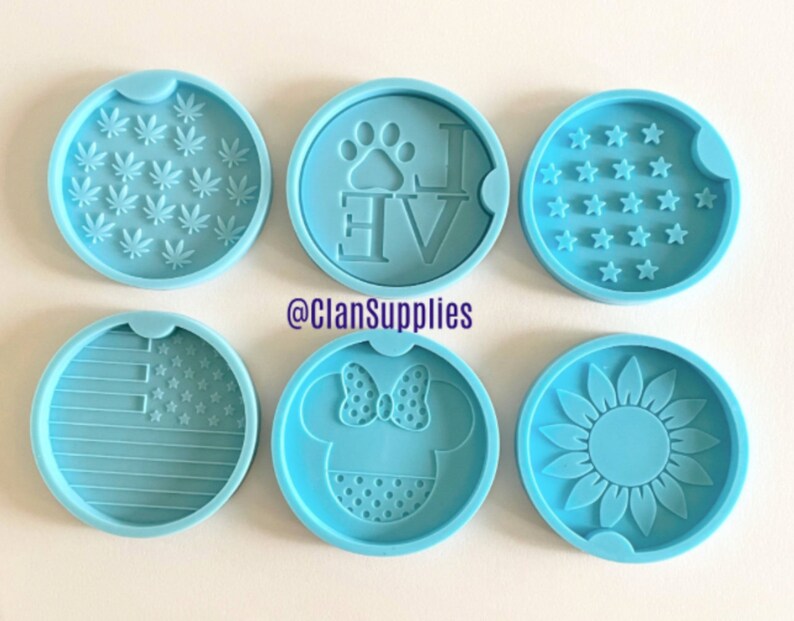 May include: Six round silicone molds for making coasters. The molds feature various designs including a paw print with the word "Love", a sunflower, a marijuana leaf, a Mickey Mouse head, an American flag, and a field of stars.