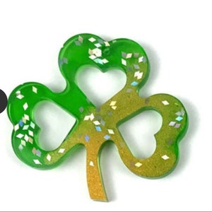 May include: A green and gold shamrock with glitter embedded in the resin. The shamrock is a popular symbol of good luck and is often used as a decoration for St. Patrick's Day.
