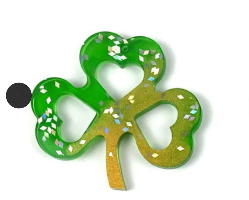 May include: A green and gold shamrock with glitter embedded in the resin. The shamrock is a popular symbol of good luck and is often used as a decoration for St. Patrick's Day.