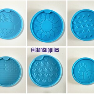 May include: Six different silicone molds for making coasters. The molds are round and blue. The designs include a sunflower, a paw print with the word "love", a marijuana leaf, a Mickey Mouse head, a US flag, and a field of stars.