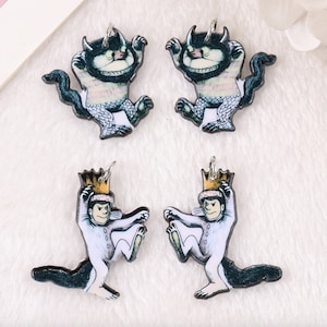 May include: Four charm pendants featuring illustrations of the character from the book Where the Wild Things Are. Two pendants feature the character in a striped suit and a crown, and two pendants feature the character in a furry suit with a toothy grin.