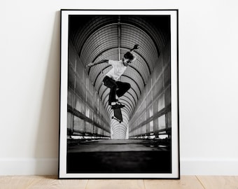 May include: Black and white photograph of a person skateboarding in a tunnel. The person is wearing a white t-shirt and black pants. The tunnel has a vaulted ceiling and is lined with metal bars.