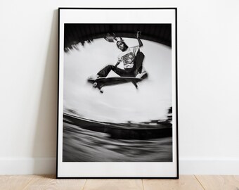 May include: Black and white photograph of a skateboarder performing a trick in mid-air. The photo is taken from a low angle, giving the viewer a sense of speed and motion. The skateboarder is wearing a t-shirt and jeans, and the skateboard is in focus.