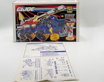 May include: A G.I. Joe Battle Corps Combat Detonator vehicle toy set in its original box. The box features a blue and orange armored vehicle with a large missile launcher. Included is an instruction sheet with diagrams.