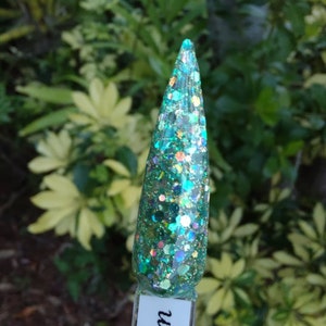May include: A close-up of a teal green nail polish with iridescent glitter. The polish is applied to a single nail tip.