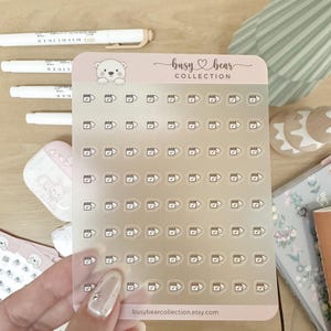 May include: Clear sticker sheet with small calendar and checkmark icons. The sticker sheet has a pink border with the text "busy bear COLLECTION" and "busybearcollection.etsy.com". White pens are in the background.