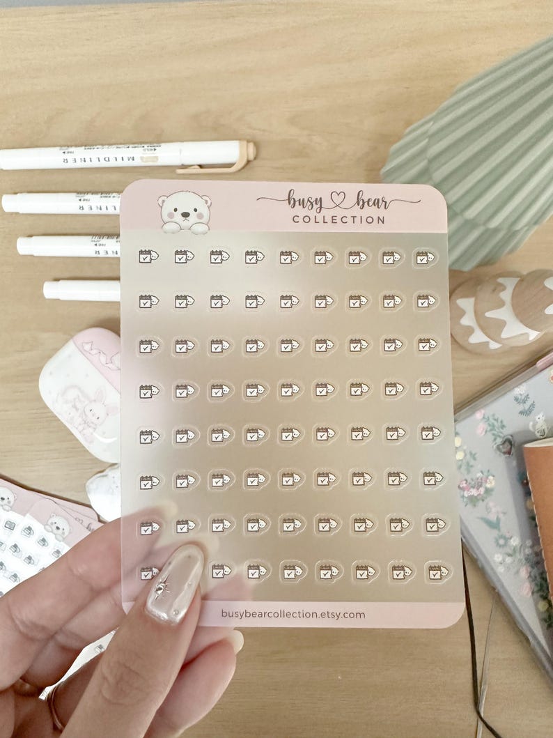 May include: Clear sticker sheet with small calendar and checkmark icons. The sticker sheet has a pink border with the text "busy bear COLLECTION" and "busybearcollection.etsy.com". White pens are in the background.