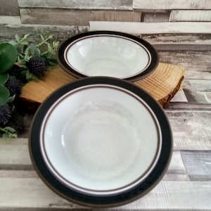 May include: Two white ceramic bowls with brown and black trim. The bowls are stacked on top of each other.