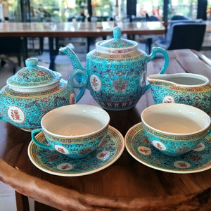May include: A turquoise blue tea set with gold trim and Chinese characters. The set includes a teapot, creamer, sugar bowl, and two teacups and saucers.