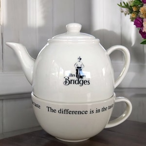 Puede incluir: Juego de tetera y taza de cerámica blanca con un logotipo en blanco y negro que dice "Mrs. Bridges" y el texto "The difference is in the taste".