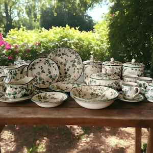 May include: A set of white and green floral patterned china dinnerware, including plates, bowls, cups, saucers, a teapot, sugar bowl, creamer, and gravy boat. The pattern features green ivy leaves on a white background.