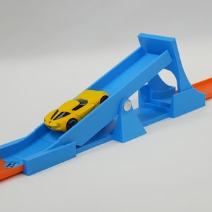 May include: A yellow toy car on a blue ramp track with an orange track extension. The car is a sports car design. The ramp has a unique design with a circular cutout. The track is designed for toy cars.
