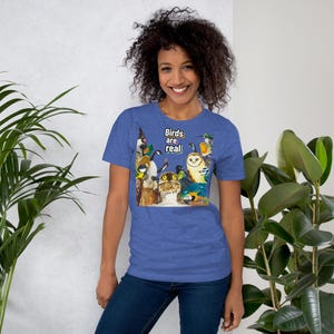 May include: Blue short-sleeve t-shirt with a colorful illustration of various birds. The text "Birds are real" is printed in white. The shirt is made of a soft material.