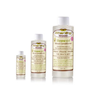 May include: Three bottles of Sterling Wood Bees-oil Wood Conditioner in different sizes. The bottles are clear and show the product inside. The label is yellow and brown with a bee illustration. The text on the label reads "Sterling Wood Bees-oil Wood Conditioner. Natural bees wax in a food-grade mineral oil base. Protects, Preserves, Beautifies. The Bee's Way!"