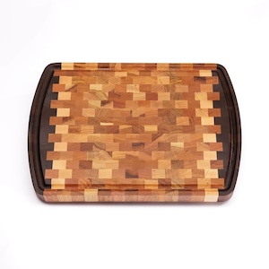 May include: A large, rectangular cutting board made of various types of wood. The board has a dark wood border and a light wood center with a checkered pattern.