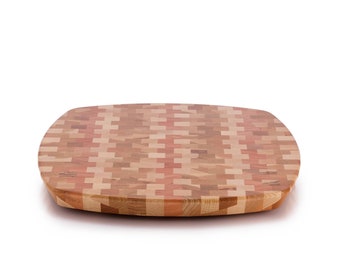 May include: Oval wooden chopping board with a mosaic pattern in light and dark wood tones. The board has rounded edges and a smooth surface, suitable for food preparation.