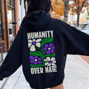 May include: Black hoodie with a graphic of flowers and the text "HUMANITY OVER HATE" on the back. The model is wearing a size XL for an oversized look.