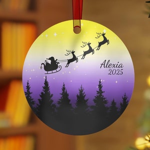 May include: A round, yellow and purple Christmas bauble featuring a silhouette of Santa Claus flying in a sleigh pulled by reindeer. The bauble has a white background with stars and the text "Alexia 2025".