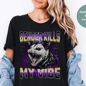 May include: Black t-shirt with a graphic of a possum and the text "Gender Kills My Vibe" in yellow and purple. The model is wearing a size XL for an oversized look.